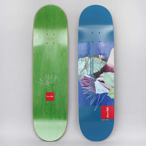 Chocolate Stevie Perez Devine Sublime Navy skateboard deck: Collage of green tropical leaves, a purple-toned figure and a white line-drawn bird of paradise flower over blue panels with thin stripes, with a red Chocolate logo block and rider name at the bottom.