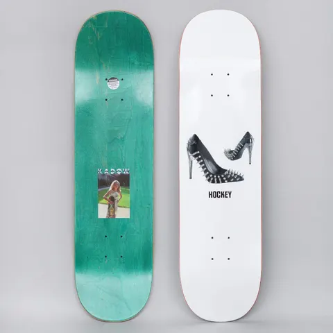 Hockey Ben Kadow Spiked Heel White skateboard deck: Pair of black high-heeled shoes studded with metal spikes, buckles and chains on a white deck, with HOCKEY in black beneath. The green underside has a small photo of a woman on a lawn.