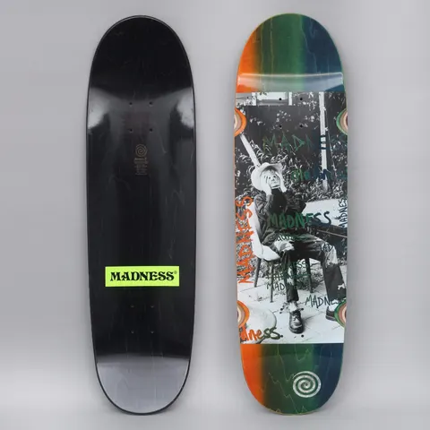 Madness Column R7 Blue / Orange skateboard deck: A black-and-white photo of a seated person in a hat covering their face with their hands, overprinted with green and blue hand-drawn Madness scrawls, on an orange-to-green-to-blue faded deck with spiral logos. The underside is black with a green Madness label.