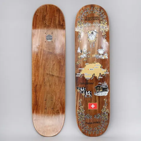Passport Tea Towel Switzerland skateboard deck: Souvenir tea-towel style print on a woodgrain-stained deck: floral wreath border, cuckoo clock, fondue, map of Switzerland with cities, cows, a chalet and a Swiss flag, in gold, black and white.