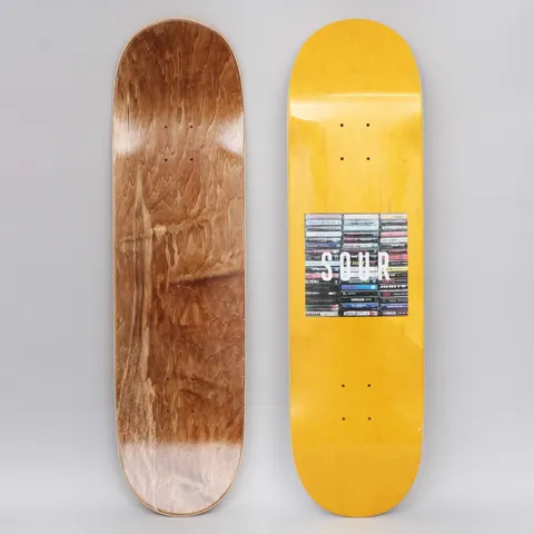 Sour Box Logo Tapes Yellow skateboard deck: Yellow-stained deck with a square photo of stacked cassette tapes and CDs and the white word SOUR across it. Brown wood underside shown alongside.