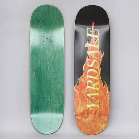 Yardsale Fuego Black skateboard deck: Realistic orange and yellow flames rising up the deck from the tail on black, with YARDSALE in large serif capitals in yellow running along the flame. Green underside has three small crosses.