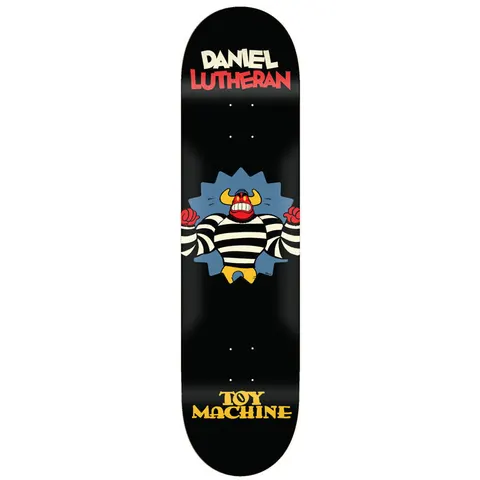 Toy Machine Daniel Lutheran Toons 8.38 skateboard deck: Cartoon horned monster in a black-and-white striped prisoner shirt bursting through a spiky blue wall with red fists raised, on a black deck. Rider name in cream and red at the top and Toy Machine logo in yellow at the bottom.
