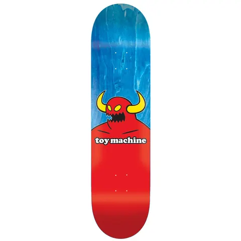 Toy Machine Monster 7.38 skateboard deck: Toy Machine red horned monster with yellow horns and jagged teeth rising from the lower half of the deck, with the brand name on a white label across its chest, over a blue wood-stained upper half.