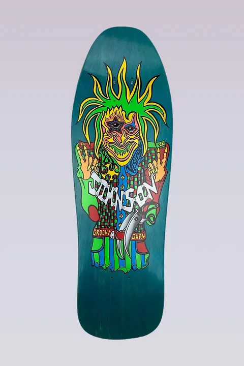 Vision Street Wear Joe Johnson Groovy Guru - Turquoise Stain skateboard deck: A psychedelic jester-like figure with spiky green and yellow hair, a three-eyed face and a checked patchwork costume, holding a curved blade. Johnson is written across its chest in jagged lettering, on a turquoise-stained old-school deck.