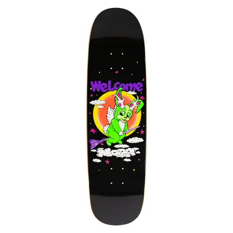 Welcome Nora Vasconcellos Full Moon on Sphynx - Black skateboard deck: Cartoon green bunny with antlers and angel wings riding a purple broomstick across a night sky of stars and clouds, in front of a glowing orange moon. Purple Welcome logo above, on a shaped black deck.